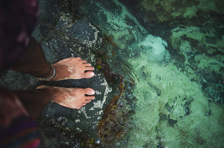Top-down view of bare feet on turquoise seawater, showing coastal hues and subtle ocean color change.