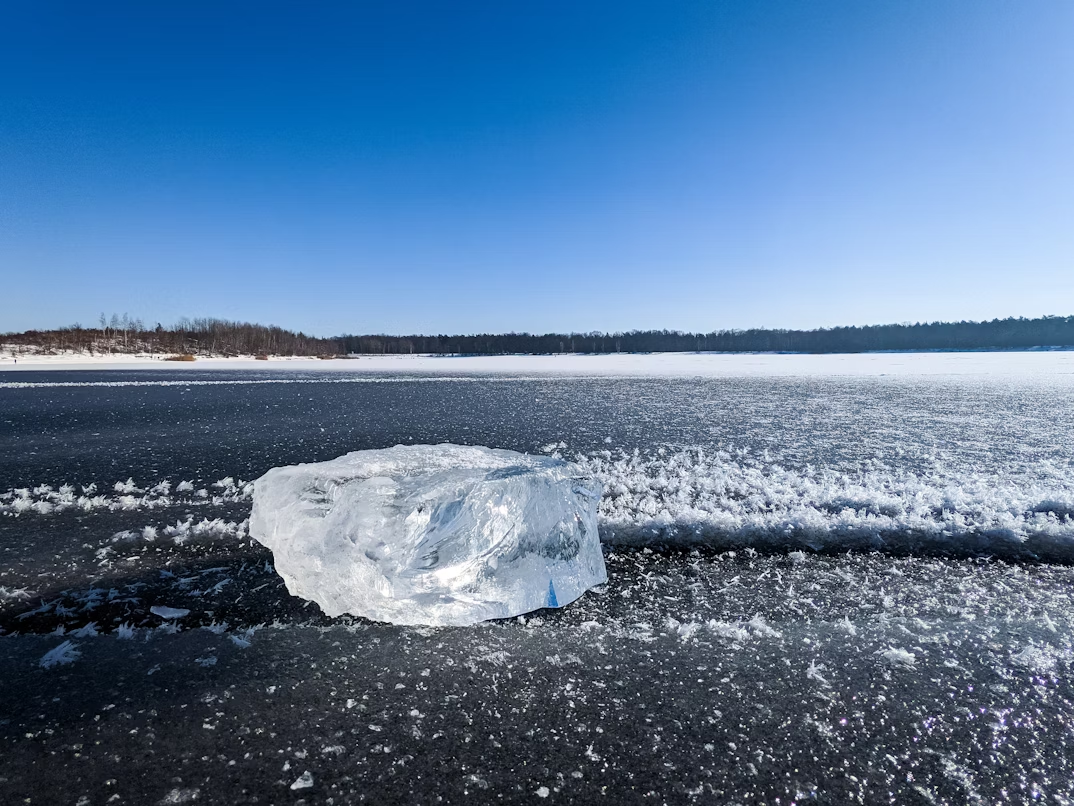 Clear block of ice on a frozen lake under a blue winter sky, symbolizing historic ice harvesting.