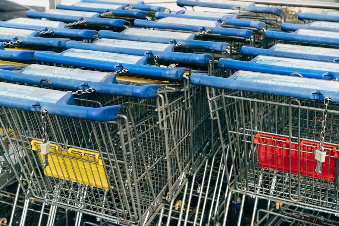 Row of blue-handled shopping carts with coin-lock chains at a supermarket entrance.