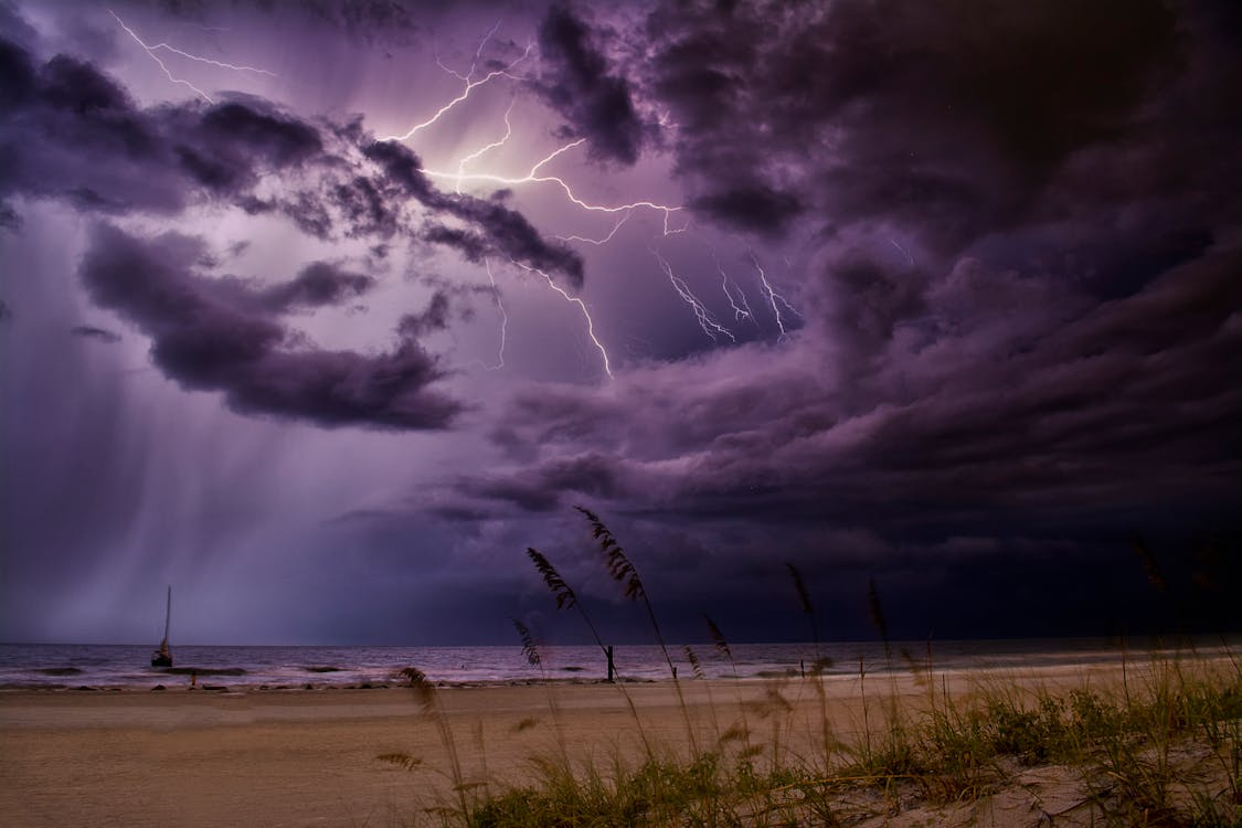 Lightning forks through purple storm clouds above a windswept beach sand at night.