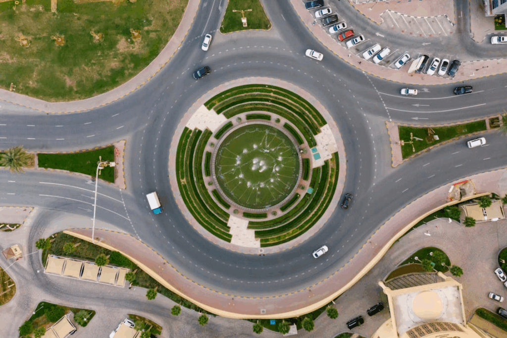 Aerial view of a multi-lane roundabout with a central fountain and cars navigating traffic.