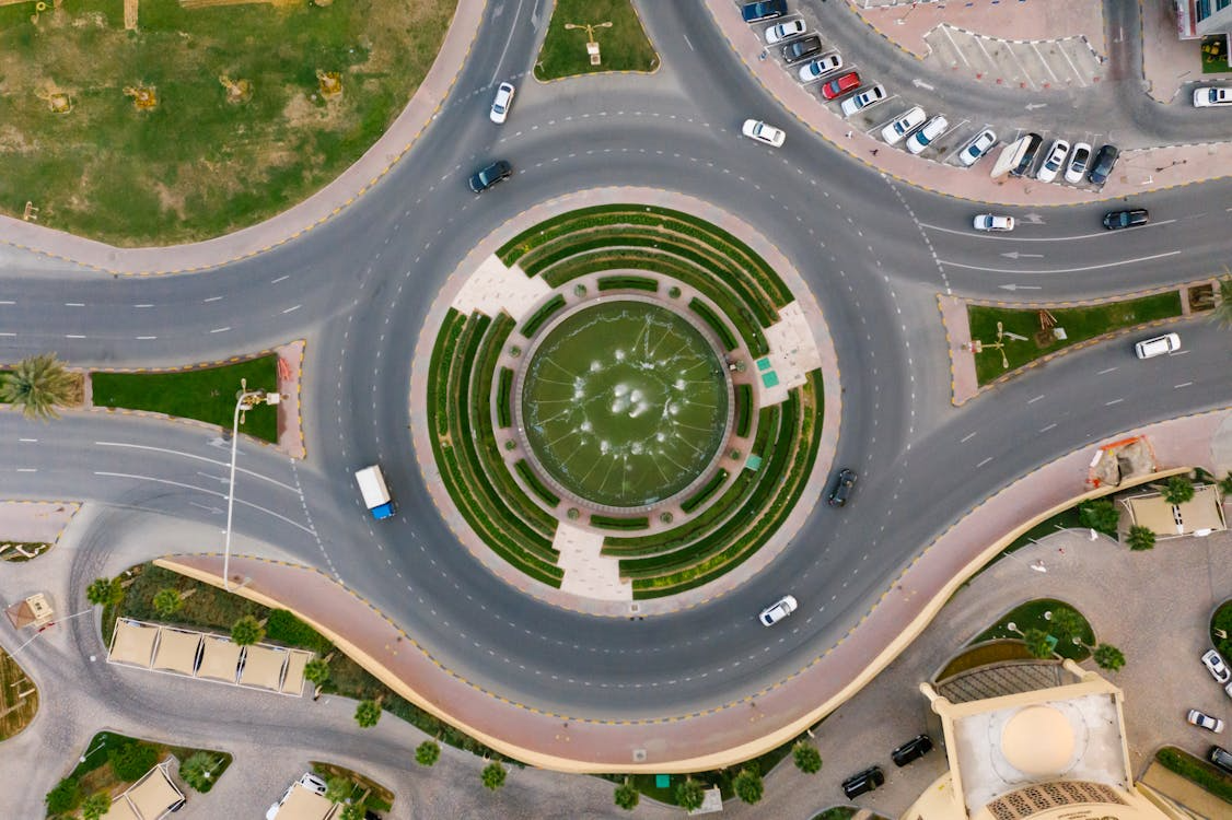Aerial view of a multi-lane roundabout with a central fountain and cars navigating traffic.