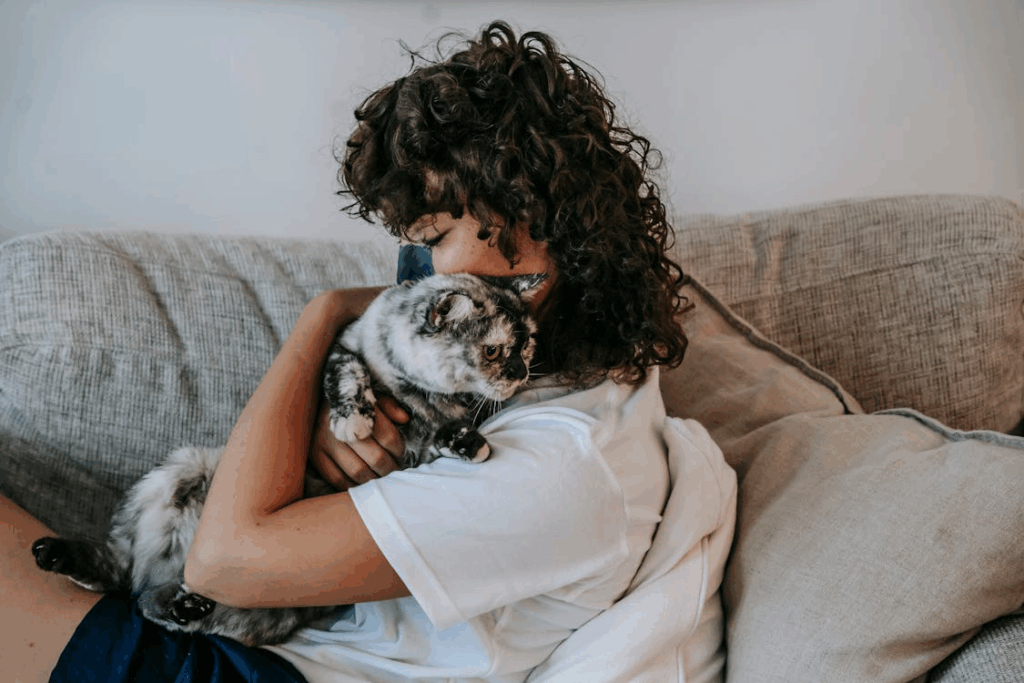 Person hugging a gray mottled cat on a sofa, showing why humans keep pets for comfort.