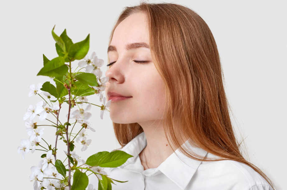 Young woman with eyes closed smelling white spring blossoms, illustrating scent memory.
