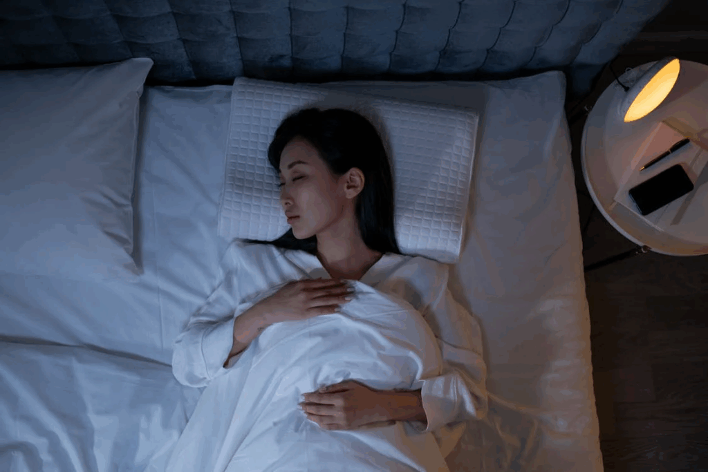 Woman sleeping on white bedding with warm bedside lamp, illustrating REM sleep and nighttime routine.